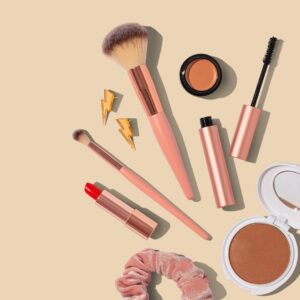 A variety of makeup and makeup brushes against a soft peach background. 